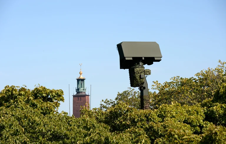 A Saab radar above the trees, with a tower in the background.